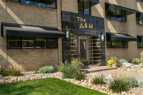 The Ash building with blonde brick construction, art deco tiled entry door, and grassy lawn.
