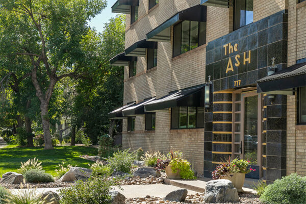 The Ash building with blonde brick construction, art deco tiled entry door, and lush landscaping.