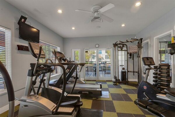 Fitness center with wall mounted TV, cardio machines, weight equipment, and large windows.