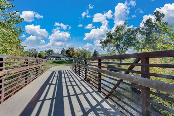 Bridge over creek lined with tall trees under cloudy blue skies.