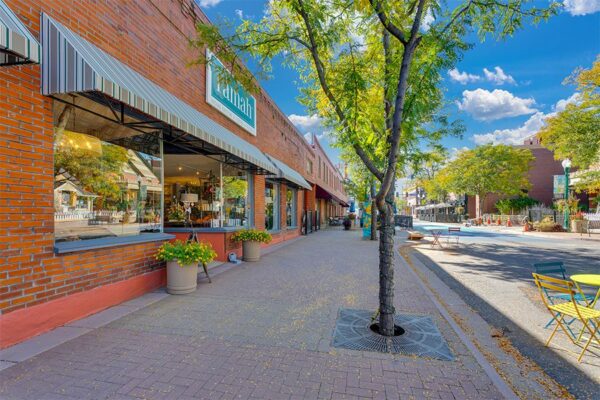 Olde Town Arvada street with stone sidewalks, storefronts, and mature trees.