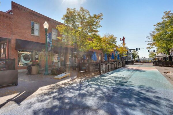 Olde Town Arvada street with sidewalk art, dining patios, and tall trees.