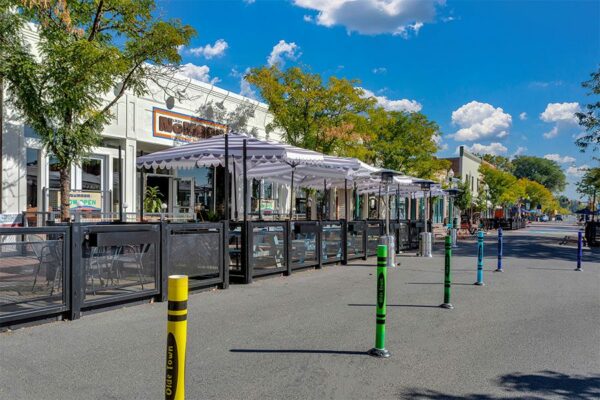 Olde Town Arvada street with outdoor patios, sidewalk art, and tall trees.