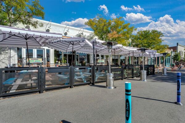 Olde Town Arvada street with dining patios, storefronts, and tall trees.