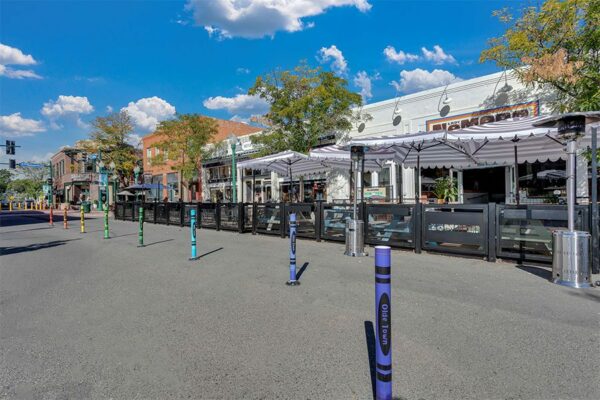 Olde Town Arvada street with dining patios, storefronts, and tall trees.