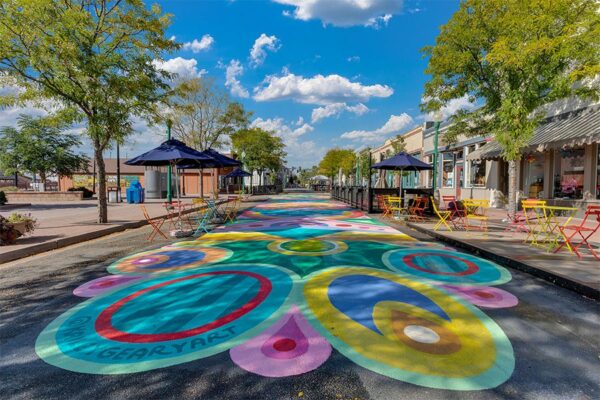 Olde Town Arvada street with sidewalk art, dining patios, and tall trees.