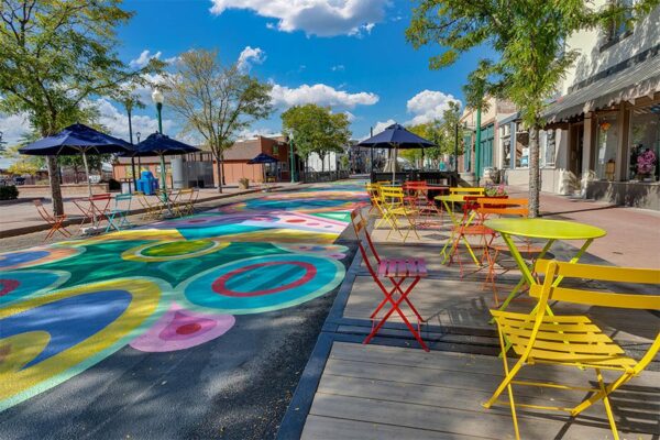 Olde Town Arvada street with sidewalk art, dining patios, and tall trees.