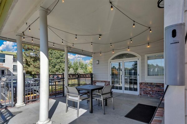 Covered patio with dining tables, string lights, and door to clubhouse.