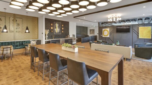 Lounge with wood floor, large dining table, comfortable lounge chairs, wall mounted TV, and artwork.