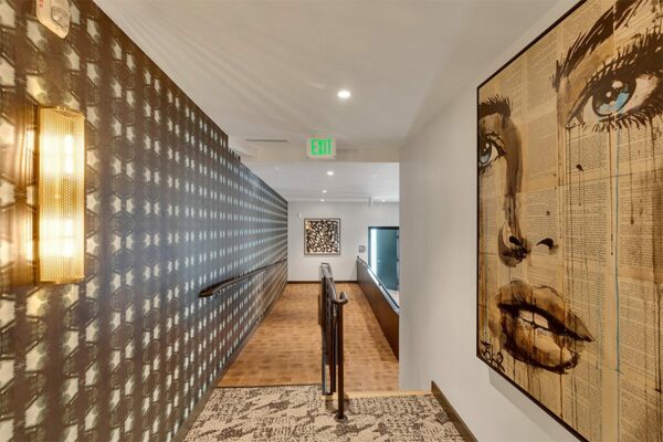 Hallway with ADA ramp, carpet and wood floors, pattern wallpaper, and large pop art piece.
