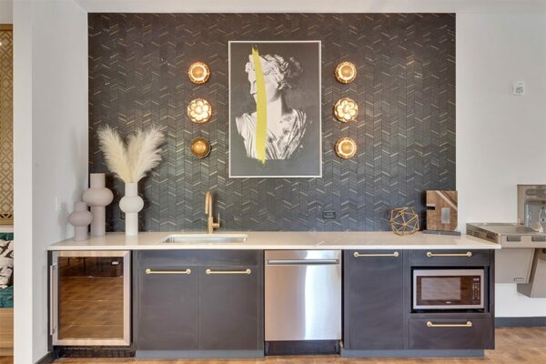 Community kitchen with stainless steel appliances, white counter, bronze faucet, and modern artwork.