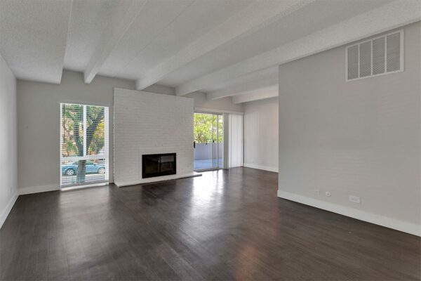 Living room with wood floor, grey walls, white brick fireplace, and sliding door to balcony.