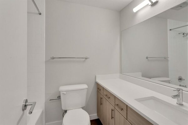 Bathroom with wood cabinets, white counters and sink, large mirror, and tiled shower tub.