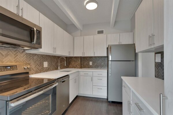 Kitchen with wood floor, light cabinets and counters, stainless steel appliances, and tiled backsplash.