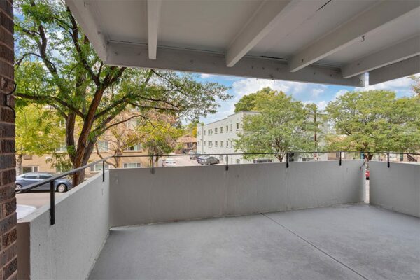 Balcony with concrete walls overlooking street with tall trees.