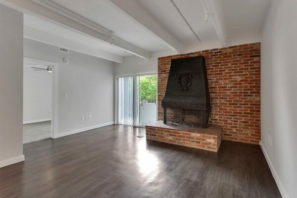 Living room with wood floor, brick accent wall with fireplace, and door to balcony.