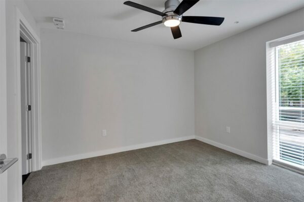 Bedroom with carpet, grey walls, ceiling fan, and large window.