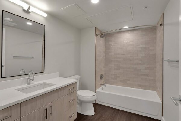 Bathroom with wood floor and cabinets, white counter, large framed mirror, and tiled shower tub.