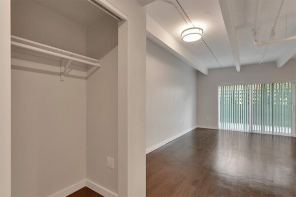 Living area with wood floor, grey walls, large closet, and door to balcony.