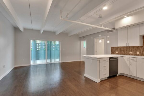 Living area with wood floor, grey walls, door to balcony, and updated kitchen.