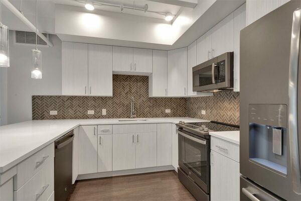 Kitchen with wood floor, light cabinets and counters, tiled backsplash, and stainless steel appliances.