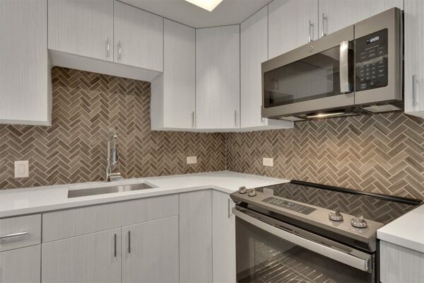 Kitchen with light cabinets and counters, stainless steel appliances, and tiled backsplash.