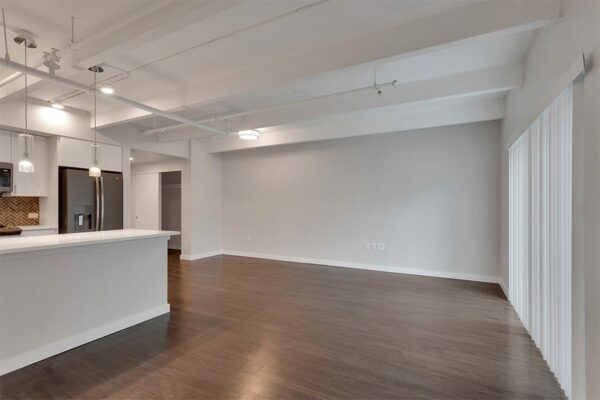 Living area with wood floor, grey walls, white trim, door to balcony, and updated kitchen.