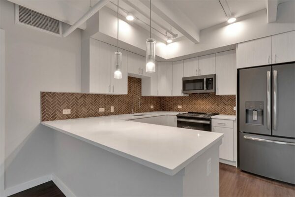 Kitchen with wood floor, light cabinets and counters, breakfast bar with pendant lights, tiled backsplash, and stainless steel appliances.