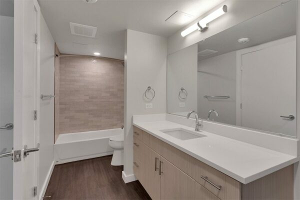 Bathroom with wood floor and cabinets, light counters, large mirror, and tiled shower tub.
