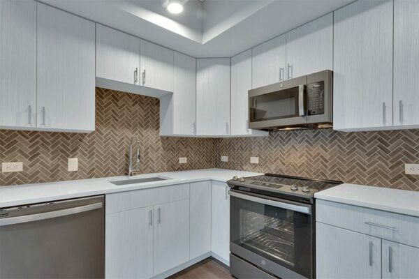 Kitchen with light cabinets and counters, stainless steel appliances, and tiled backsplash.