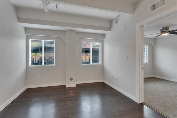 Living area with wood floor, grey walls, white trim, large windows, and door to bedroom.