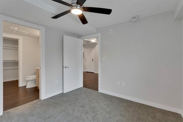 Bedroom with carpet, grey walls, white trim, ceiling fan, and doors to living room and bathroom.