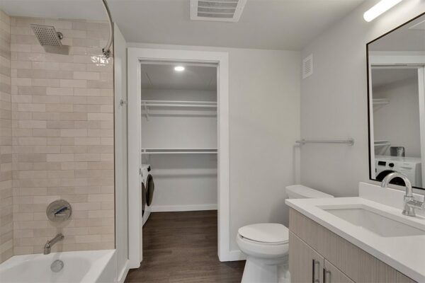 Bathroom with wood floor and cabinets, framed mirror, tiled shower tub, and door to closet.