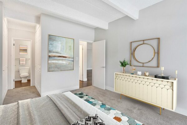 Bedroom with carpet, geometric rug, mid century modern furniture, and doors to hallway and bathroom.