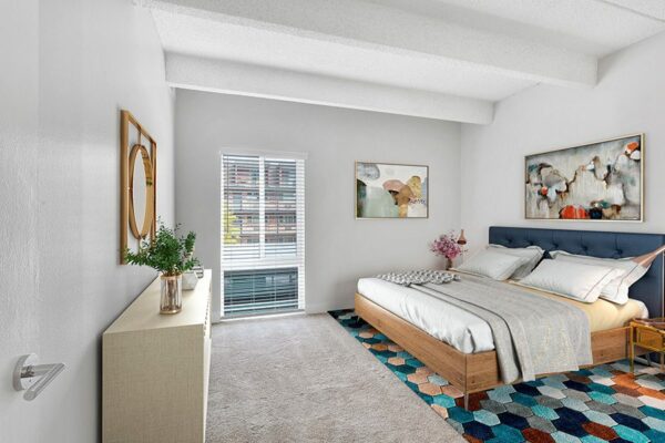 Bedroom with plush carpet, bed with headboard, framed art, and large window.
