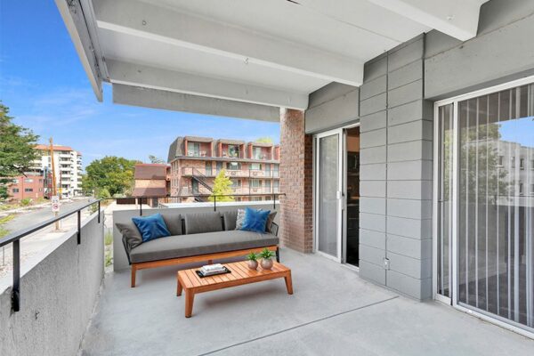 Balcony with plush outdoor furniture, sliding door to apartment, and railing overlooking street.