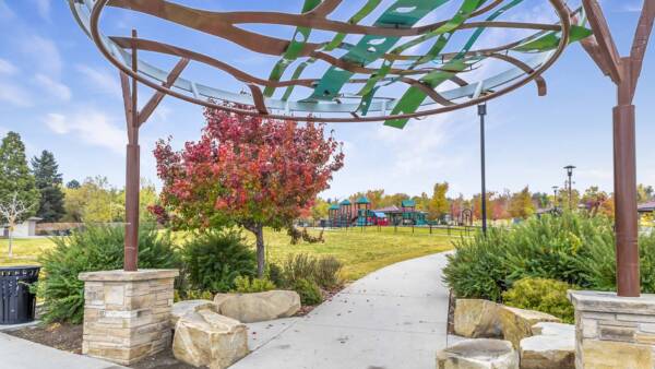 Wheat Ridge park with grassy lawns, playground equipment, lush landscaping, and large sculpture.
