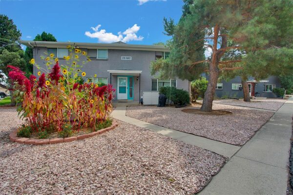 Trace Townhomes with rocky landscaping, large shrubs, mature trees, and concrete paths.