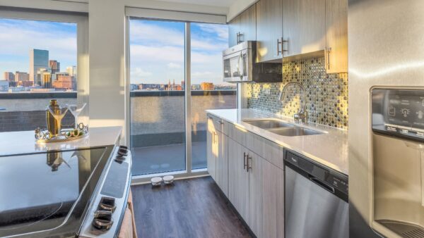 large kitchen with island counter, oven, sink, fridge and large windows overlooking the balcony.