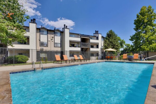 large swimming pool with orange accent chairs and apartment buildings behind