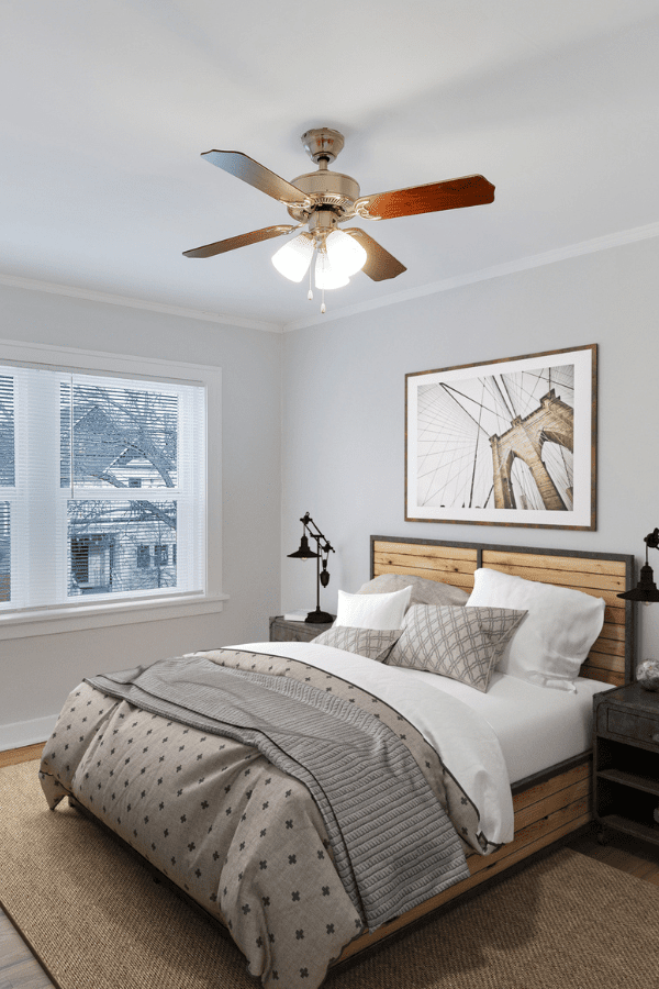bedroom with bed in the middle, wooden headboard, night stands, large window and ceiling fan.