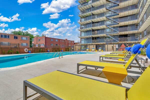 Pool area with yellow lounge chairs overlooked by apartment balconies.
