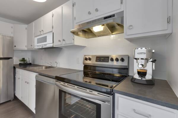 Kitchen with wood floor, white cabinets, grey counters, and stainless steel appliances.