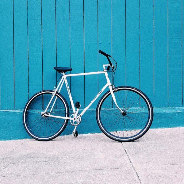 Single speed bike leaning against bright blue painted fence.