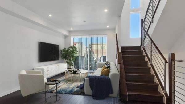Rendering of stairs leading down into a living room with wood floors and patio doors.