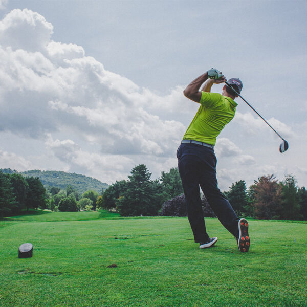 Person at golf course in green shirt swinging golf club under cloudy skies.