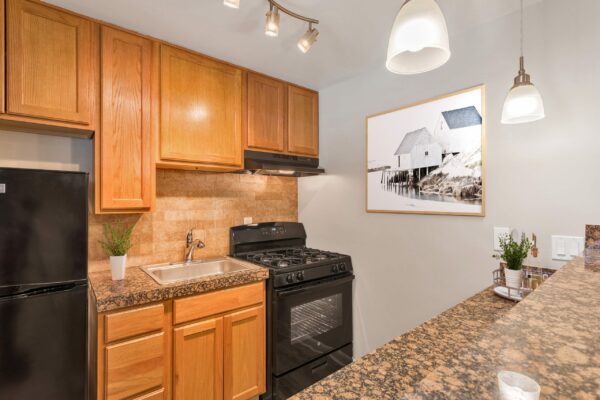 Kitchen with wood cabinets, stone counters, black appliances, and pendant lights.