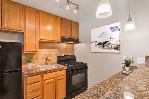Kitchen with wood cabinets, stone counters, black appliances, and framed artwork.