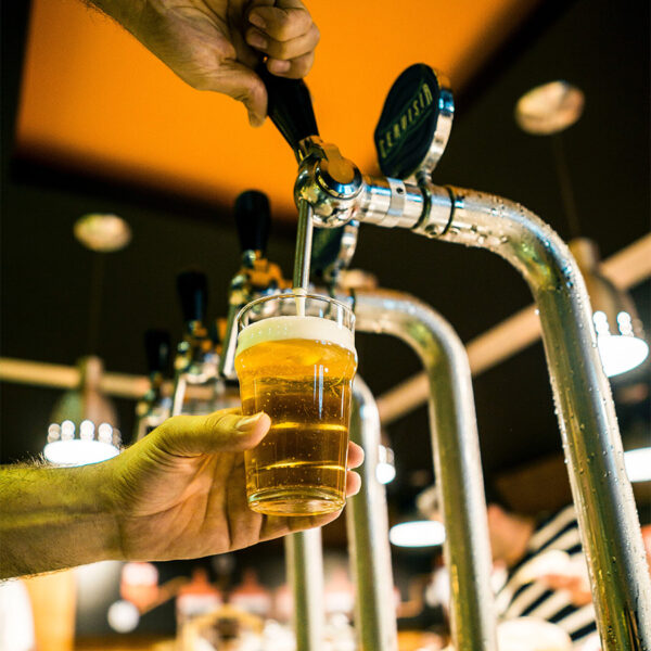 Person pouring light golden beer into glass from metal tap.