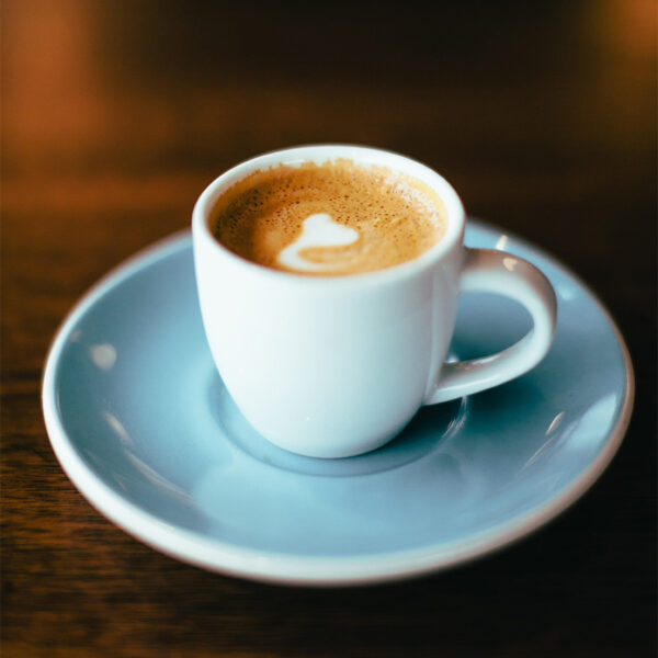 Detail of cappuccino with light blue saucer on dark wood table.